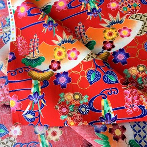 May include: Red fabric with a floral and wave pattern. The fabric features a variety of colors, including blue, green, yellow, and white. The fabric is folded in half, and the pattern is visible on both sides.