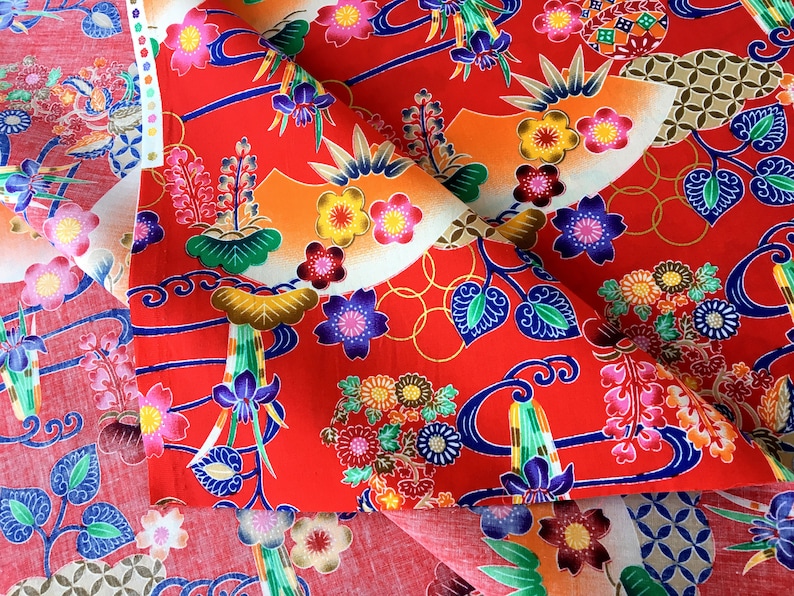 May include: Red fabric with a floral and wave pattern. The fabric features a variety of colors, including blue, green, yellow, and white. The fabric is folded in half, and the pattern is visible on both sides.