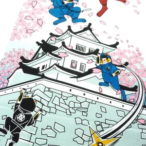 May include: A fabric print featuring cartoon cats dressed as ninjas in blue, red, and black outfits. The cats are depicted climbing a white Japanese castle wall and jumping through the air amidst falling pink cherry blossom petals and a yellow shuriken.