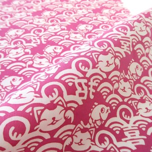 Pu&ograve; includere: Un tessuto color magenta vivace con un motivo ripetitivo di gatti portafortuna, pesci e onde stilizzate in bianco. Il design include piccoli caratteri cinesi bianchi intervallati tra i gatti e i pesci, creando una stampa grafica densa e continua sull'intera superficie del tessuto.