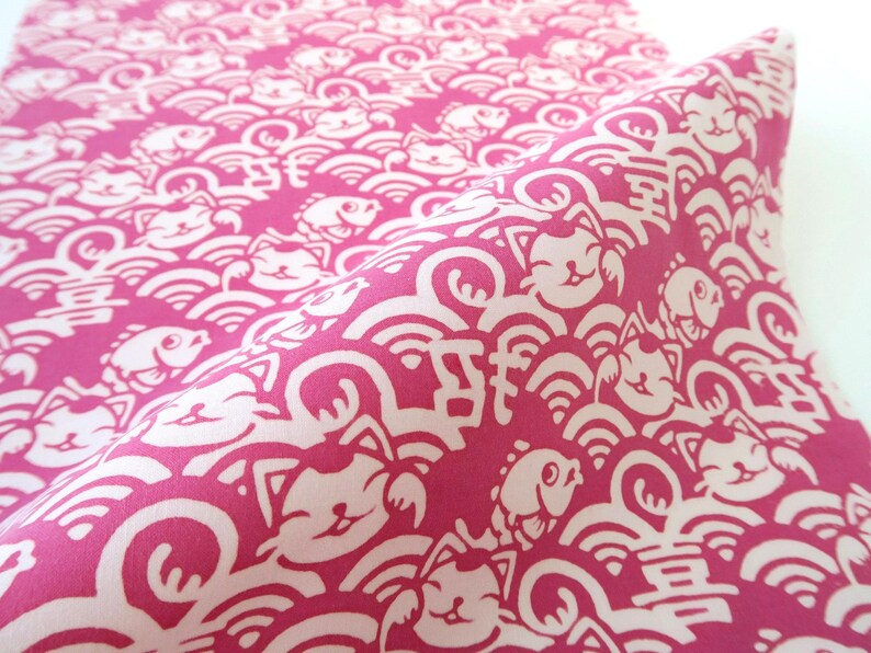 Pu&ograve; includere: Un tessuto color magenta vivace con un motivo ripetitivo di gatti portafortuna, pesci e onde stilizzate in bianco. Il design include piccoli caratteri cinesi bianchi intervallati tra i gatti e i pesci, creando una stampa grafica densa e continua sull'intera superficie del tessuto.