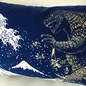 May include: A blue pillow with a white wave and a mountain design. A large, gray, Godzilla-like monster is emerging from the wave.
