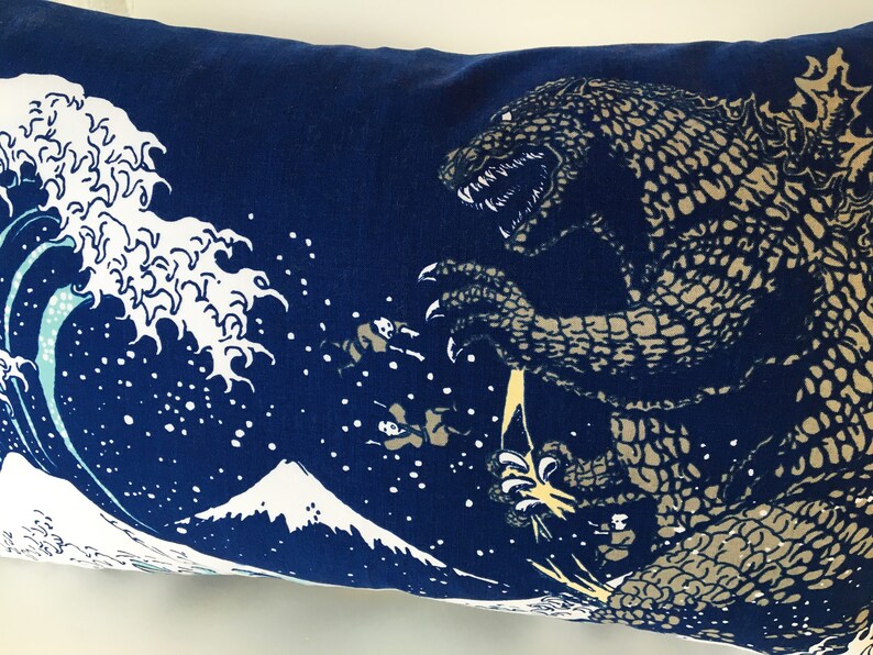 May include: A blue pillow with a white wave and a mountain design. A large, gray, Godzilla-like monster is emerging from the wave.