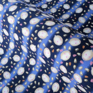 May include: Close-up of a fabric with a repeating pattern of white, oval-shaped designs with pink accents, scattered across a dark blue background with blue stripes. Small orange and pink shapes are also present.