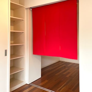 May include: A white room with a closet on the left and a red curtain covering a doorway on the right. The floor is made of wood.