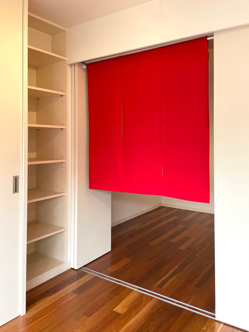 May include: A white room with a closet on the left and a red curtain covering a doorway on the right. The floor is made of wood.