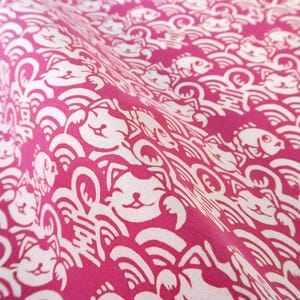 Pu&ograve; includere: Un tessuto rosa vivace con un motivo ripetuto di gatti portafortuna bianchi, pesci stilizzati e onde. Il design include piccoli caratteri kanji intervallati tra i gatti e i pesci, creando una stampa grafica densa e continua.