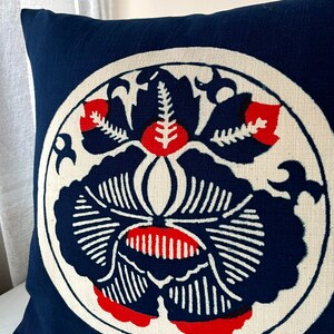 Op de afbeelding: Een blauw kussen met een witte cirkel in het midden. De cirkel heeft een rood en blauw bloemenmotief.