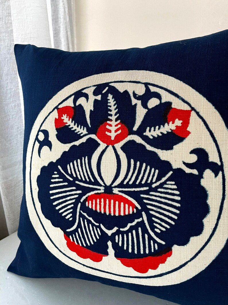 Op de afbeelding: Een blauw kussen met een witte cirkel in het midden. De cirkel heeft een rood en blauw bloemenmotief.