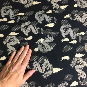 May include: Black fabric with a repeating pattern of white dragons and clouds. The fabric is textured and has a subtle sheen.