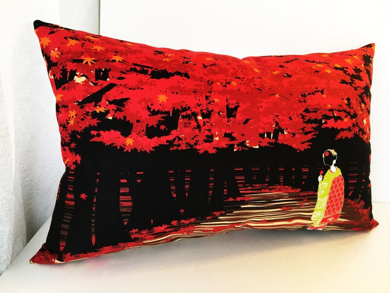 May include: Red and black pillow with a Japanese-inspired design featuring a woman in a kimono walking through a forest of red maple trees.