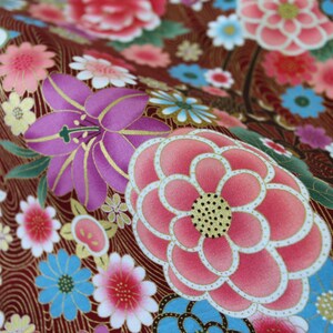 May include: A fabric featuring a deep maroon background with a gold-toned wavy line pattern. The surface is covered in a dense floral print with large pink and purple blossoms, smaller light blue and white flowers, and green leaves with gold outlines.