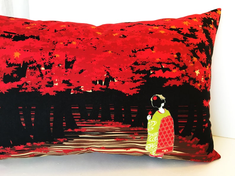 May include: A red and black pillow with a Japanese-inspired design. The pillow features a woman in a traditional kimono standing in a forest of red maple trees.