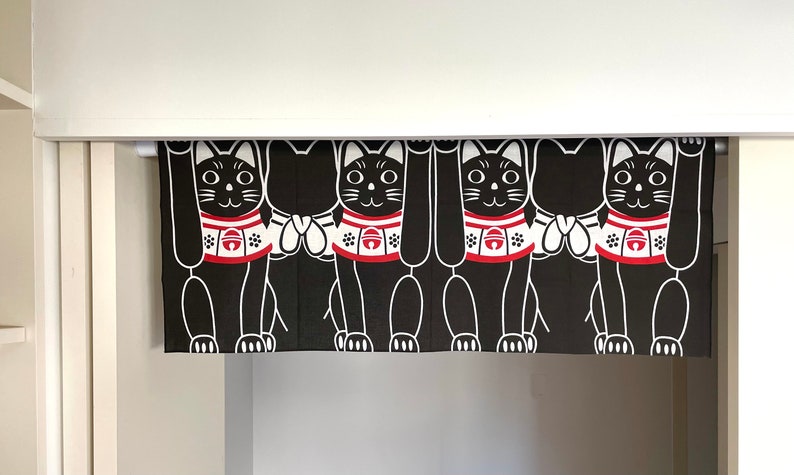 Puede incluir: Cortina Maneki Neko en blanco y negro con cuatro gatos de la suerte estilizados con las patas levantadas. Cada gato tiene un collar rojo con una campana y detalles blancos. La cortina cuelga en una puerta.