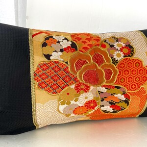 Pode incluir: Uma almofada preta com uma borda dourada e um design floral de inspira&ccedil;&atilde;o japonesa colorido. O design apresenta flores vermelhas, laranja, douradas e brancas, bem como padr&otilde;es geom&eacute;tricos.