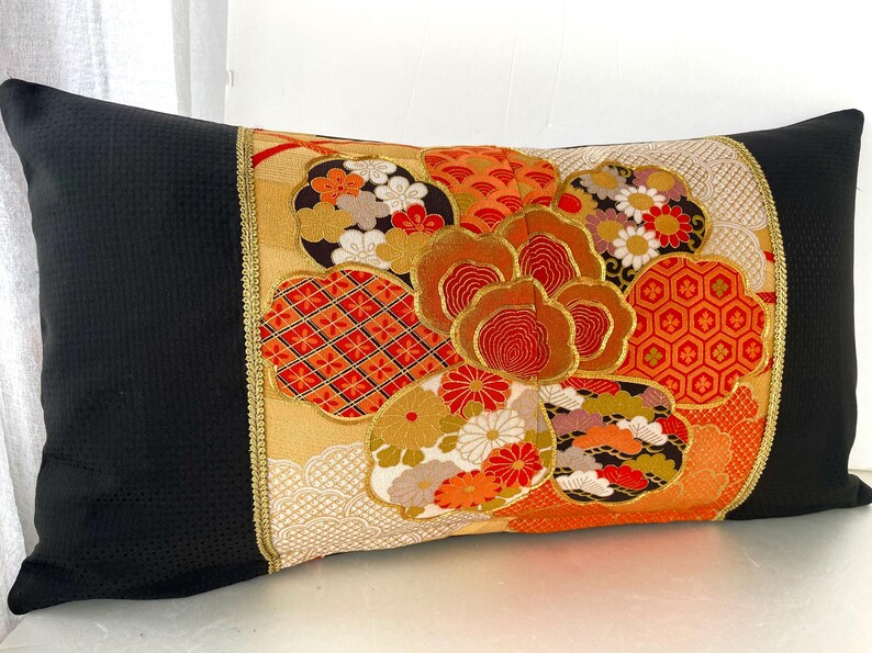 Pode incluir: Uma almofada preta com uma borda dourada e um design floral de inspira&ccedil;&atilde;o japonesa colorido. O design apresenta flores vermelhas, laranja, douradas e brancas, bem como padr&otilde;es geom&eacute;tricos.