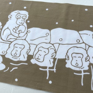 May include: A brown and white textile featuring a repeating pattern of cartoon monkeys. The monkeys are depicted in a simple, line-art style, with some holding babies. White dots are scattered across the background.