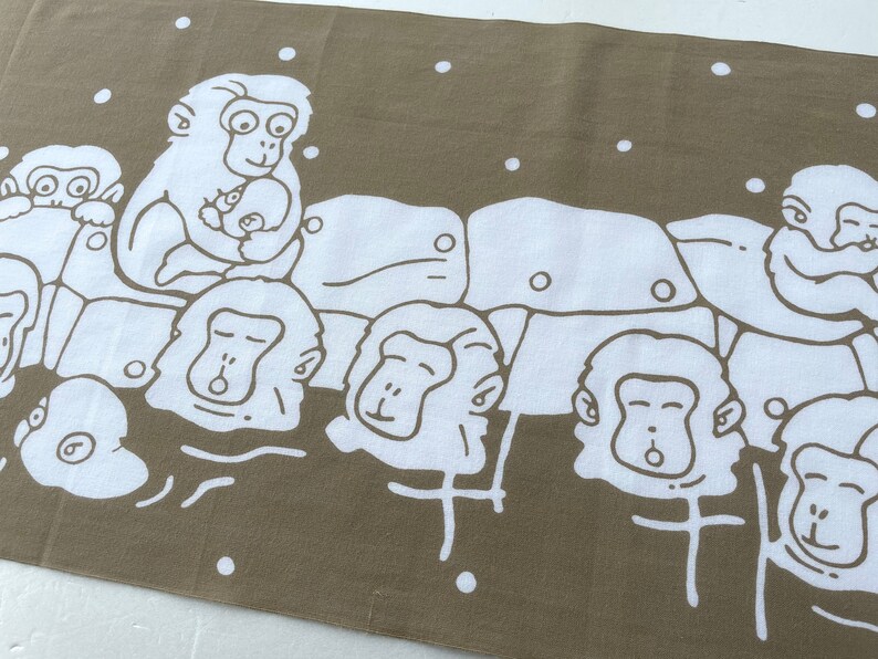 May include: A brown and white textile featuring a repeating pattern of cartoon monkeys. The monkeys are depicted in a simple, line-art style, with some holding babies. White dots are scattered across the background.