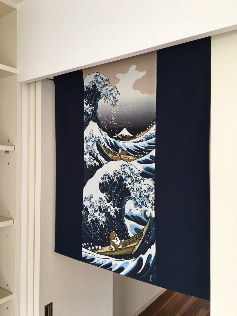 May include: A blue and white tapestry featuring a large wave with a boat and a small figure in the foreground. The wave is reminiscent of the Great Wave off Kanagawa by Hokusai. The tapestry is hanging on a white wall.