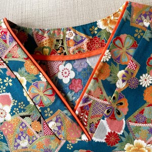 Puede incluir: Una tela azul turquesa con un estampado floral colorido. La tela tiene un ribete naranja contrastante alrededor del escote.