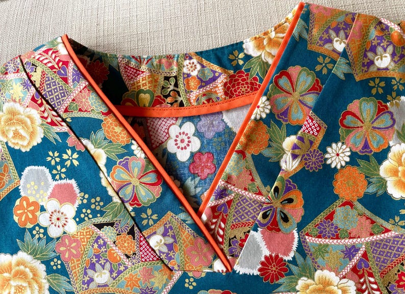 Puede incluir: Una tela azul turquesa con un estampado floral colorido. La tela tiene un ribete naranja contrastante alrededor del escote.