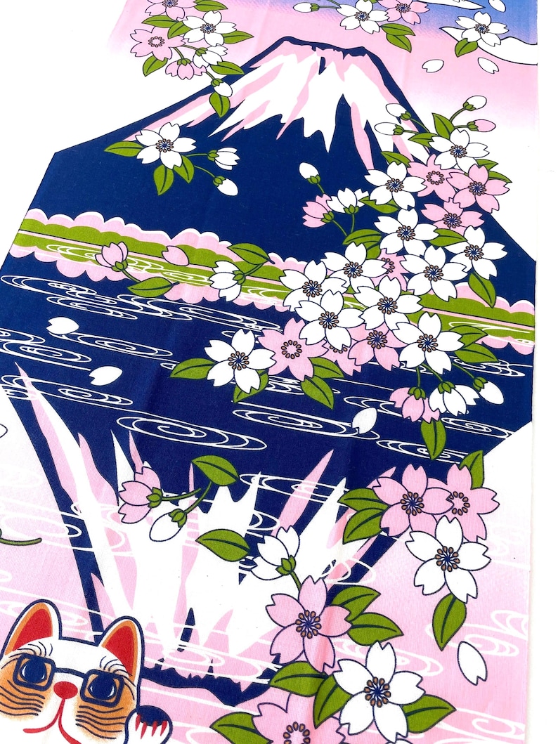 May include: A fabric textile featuring a graphic print of Mount Fuji in dark blue with a white snow-capped peak, surrounded by pink and white cherry blossoms, green leaves, and stylized water waves, with a cat wearing glasses at the bottom.