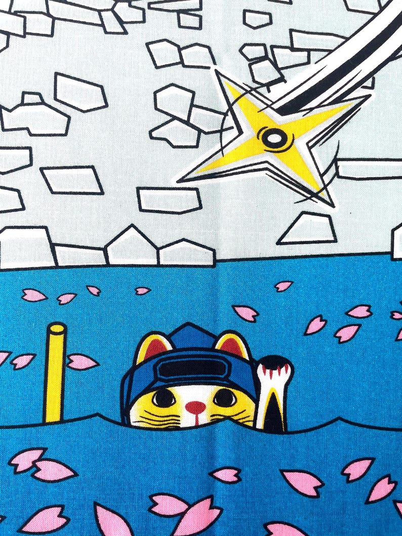 May include: A fabric print featuring a yellow and white cat wearing a blue ninja hood, emerging from blue water scattered with pink cherry blossom petals. Above, a yellow shuriken flies against a light gray background with stone-like shapes.