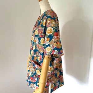 Puede incluir: Una camisa de manga corta azul turquesa con un estampado floral colorido. La camisa tiene cuello en V y dos bolsillos en la parte delantera.
