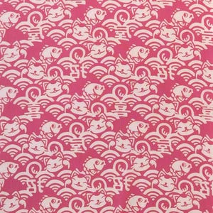 Pu&ograve; includere: Un tessuto rosa vivace con un motivo bianco ripetuto di gatti portafortuna stilizzati, pesci e onde. Il design include piccoli caratteri cinesi integrati nei motivi a onde, creando una stampa grafica densa e continua su tutto il tessuto.