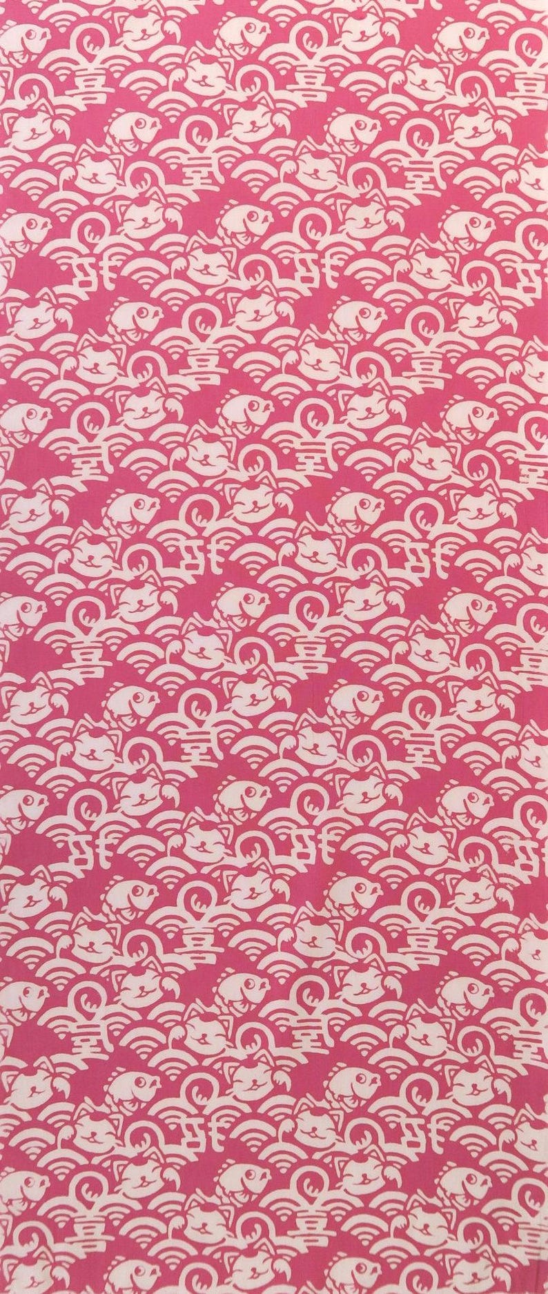 Pu&ograve; includere: Un tessuto rosa vivace con un motivo bianco ripetuto di gatti portafortuna stilizzati, pesci e onde. Il design include piccoli caratteri cinesi integrati nei motivi a onde, creando una stampa grafica densa e continua su tutto il tessuto.