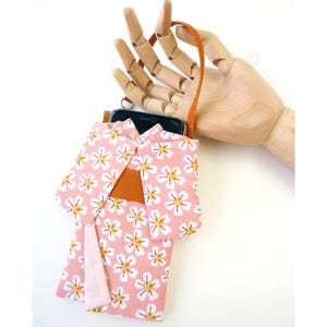 May include: A pink fabric phone pouch designed to resemble a kimono, featuring a white and yellow cherry blossom pattern. The pouch includes a solid orange obi-style band across the middle and a light pink fabric accent hanging from the side.