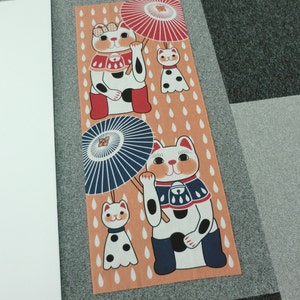 May include: A tan fabric panel with a repeating pattern of raindrops. Three white cats with black spots are holding umbrellas. The cats are wearing red, blue, and black clothing.