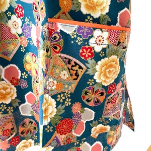 Puede incluir: Tela azul turquesa con un patr&oacute;n floral en tonos de rosa, amarillo, naranja y morado. La tela tiene un bolsillo con un ribete naranja.