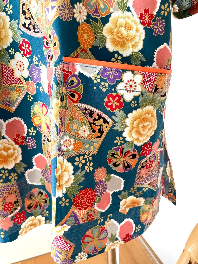 Puede incluir: Tela azul turquesa con un patr&oacute;n floral en tonos de rosa, amarillo, naranja y morado. La tela tiene un bolsillo con un ribete naranja.