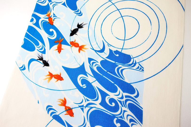 K&ouml;nnte beinhalten: Ein wei&szlig;er Stoff mit einem grafischen Druck von orangefarbenen und schwarzen Goldfischen, die zwischen stilisierten blauen Wasserwellen und konzentrischen kreisf&ouml;rmigen Wellen schwimmen. Das Design bedeckt die Oberfl&auml;che mit flie&szlig;enden Linien.