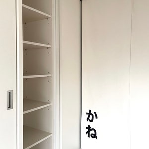 Puede incluir: Un armario blanco con puertas correderas. El armario tiene estantes en el lado izquierdo y una puerta blanca con la palabra japonesa "ka" en el lado derecho.