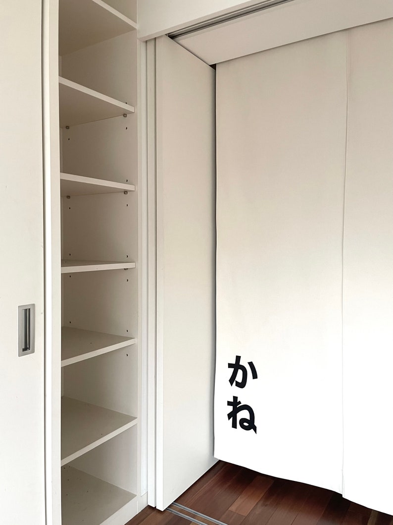 Puede incluir: Un armario blanco con puertas correderas. El armario tiene estantes en el lado izquierdo y una puerta blanca con la palabra japonesa "ka" en el lado derecho.
