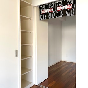 Puede incluir: Vista interior de una habitaci&oacute;n con un armario blanco y una puerta. Una cortina negra con ilustraciones de gatos blancos cuelga en la puerta. La habitaci&oacute;n tiene pisos de madera.