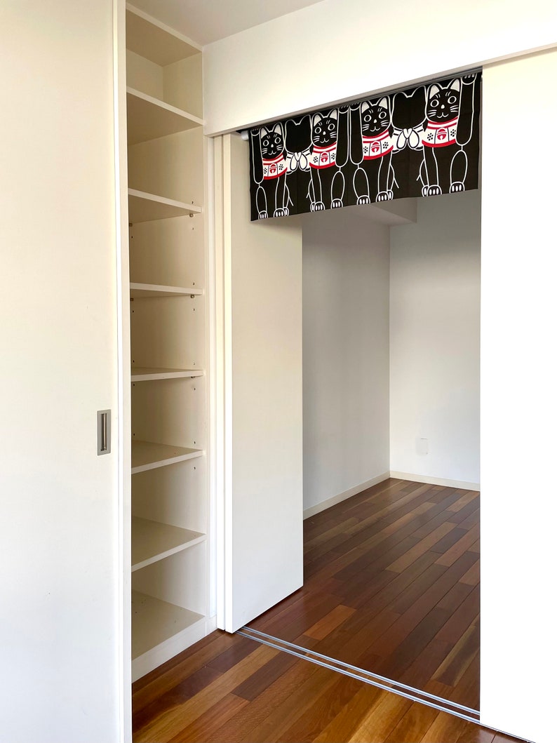 Puede incluir: Vista interior de una habitaci&oacute;n con un armario blanco y una puerta. Una cortina negra con ilustraciones de gatos blancos cuelga en la puerta. La habitaci&oacute;n tiene pisos de madera.