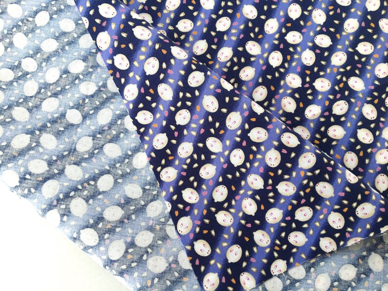 May include: Two fabric swatches with a repeating pattern of white lemon-like shapes on a navy blue background. One swatch is a lighter blue with the same pattern. The fabric has a diagonal striped design.