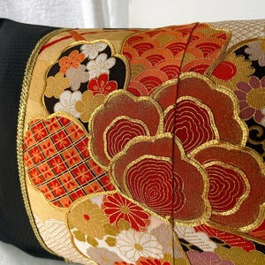 Pode incluir: Uma almofada preta com uma borda dourada e um design de tecido de estilo japon&ecirc;s colorido com flores vermelhas, laranja, douradas e brancas e padr&otilde;es geom&eacute;tricos.