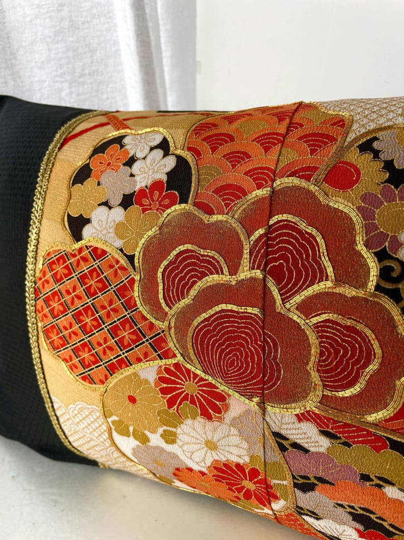 Pode incluir: Uma almofada preta com uma borda dourada e um design de tecido de estilo japon&ecirc;s colorido com flores vermelhas, laranja, douradas e brancas e padr&otilde;es geom&eacute;tricos.
