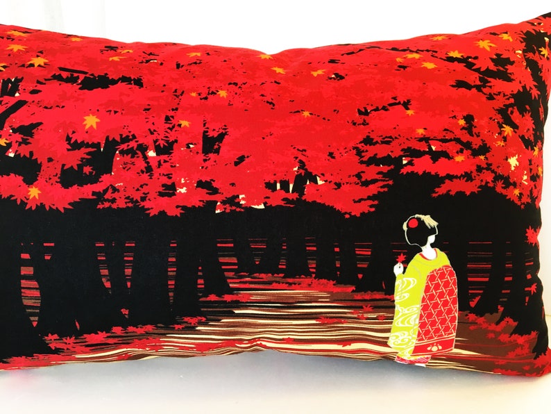 May include: A red and black throw pillow with a Japanese-inspired design. The pillow features a woman in a traditional kimono standing in a forest of red maple trees.
