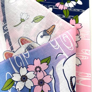 May include: A folded textile featuring a multi-layered design with navy blue, white, and pink sections. The fabric displays printed illustrations of white cherry blossoms with pink centers, green leaves, and a white swan with a black and orange beak.