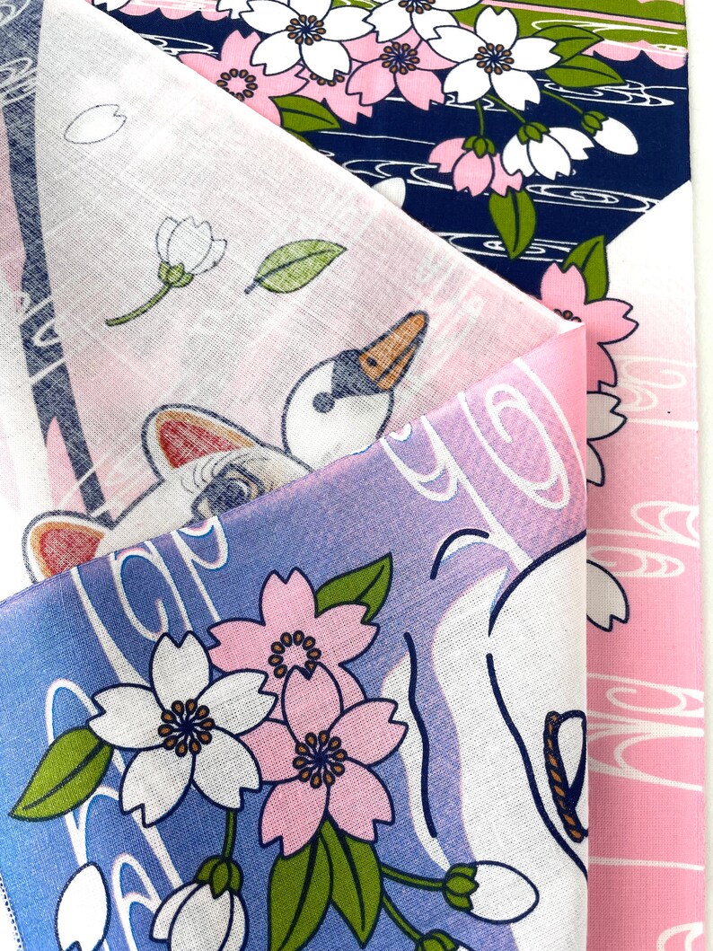 May include: A folded textile featuring a multi-layered design with navy blue, white, and pink sections. The fabric displays printed illustrations of white cherry blossoms with pink centers, green leaves, and a white swan with a black and orange beak.