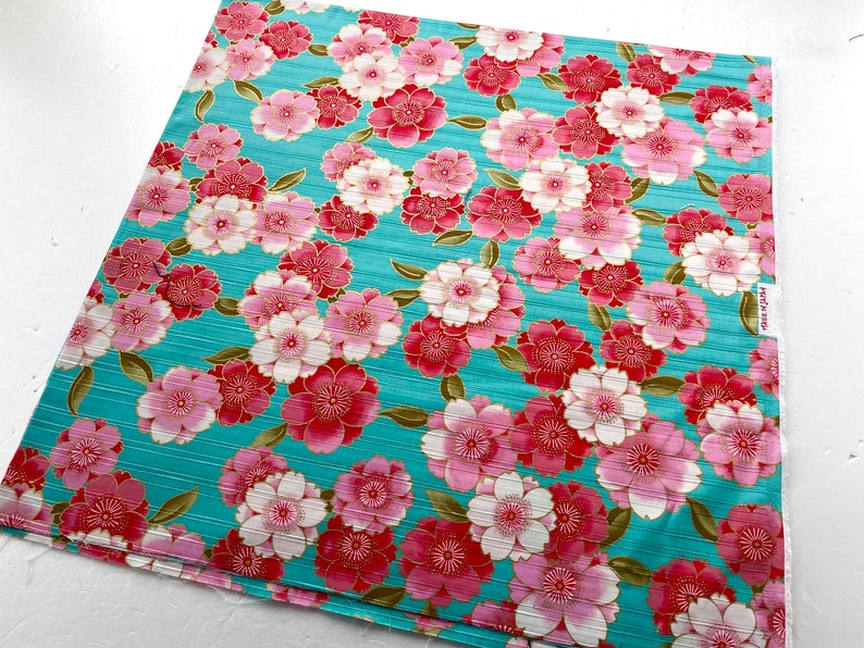 May include: Teal fabric with a repeating pattern of pink and red flowers with gold accents. The fabric has a subtle striped texture.