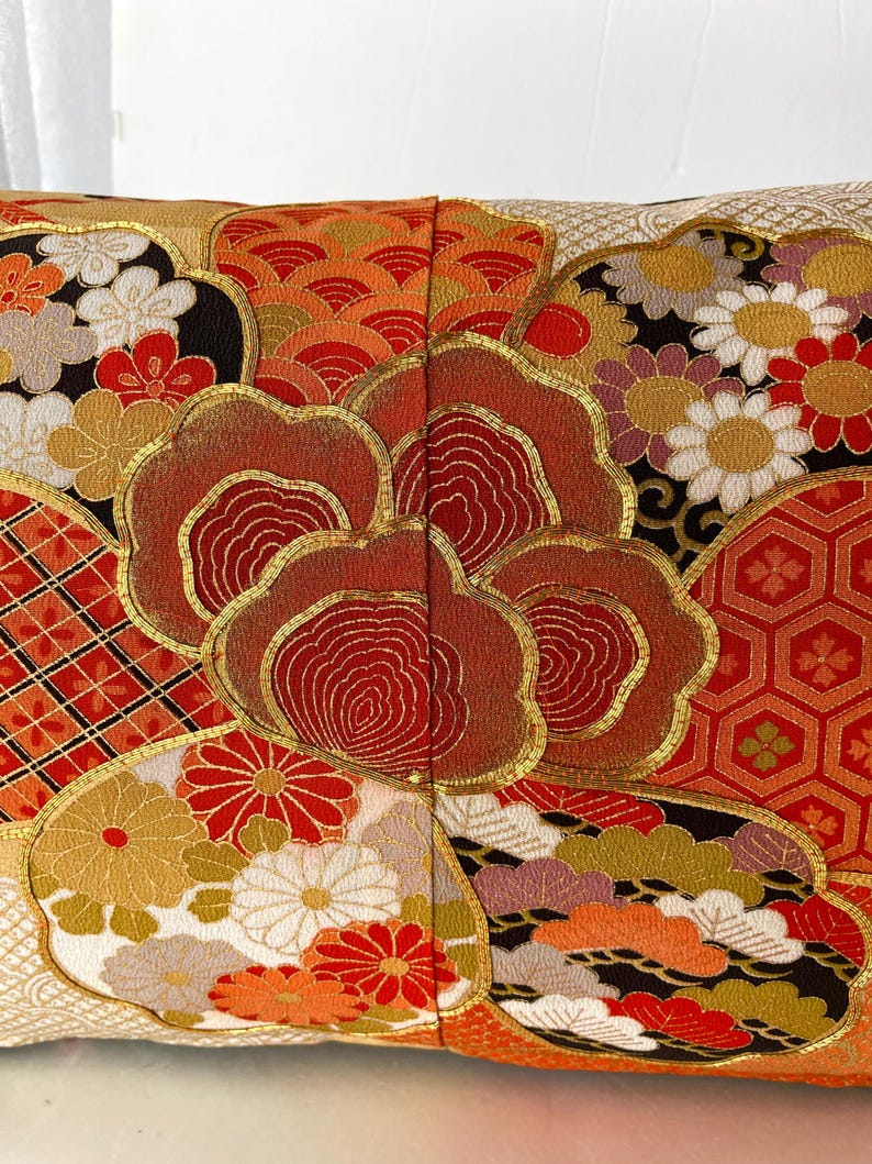 Pode incluir: Uma almofada retangular com um padr&atilde;o de inspira&ccedil;&atilde;o japonesa em vermelho, dourado e branco. A almofada &eacute; feita de um tecido macio e luxuoso e apresenta uma variedade de desenhos intrincados, incluindo flores, nuvens e formas geom&eacute;tricas.