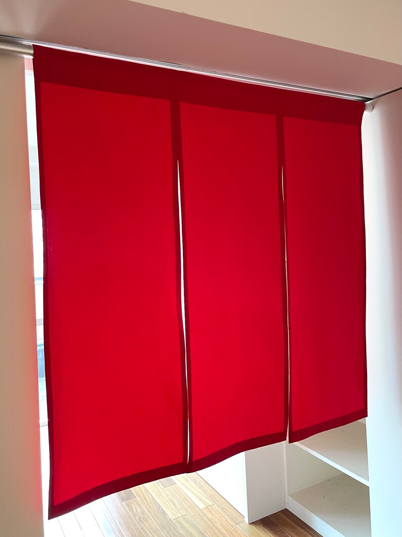 May include: Three red fabric panels with a dark red border hang from a track. The panels are closed, blocking the view behind them.