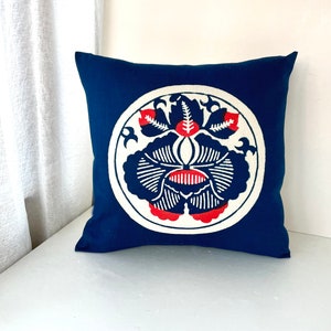 Op de afbeelding: Een blauw kussen met een wit cirkelvormig ontwerp met een rood en blauw bloemenpatroon.