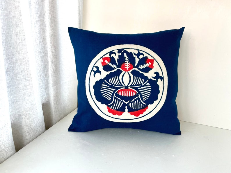 Op de afbeelding: Een blauw kussen met een wit cirkelvormig ontwerp met een rood en blauw bloemenpatroon.